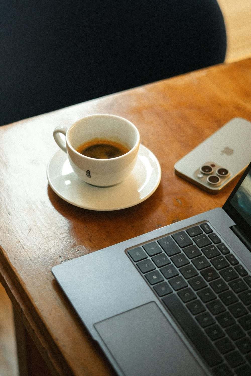 Meja kayu dengan laptop, ponsel, dan secangkir kopi sebagai lambang membaca informasi digital